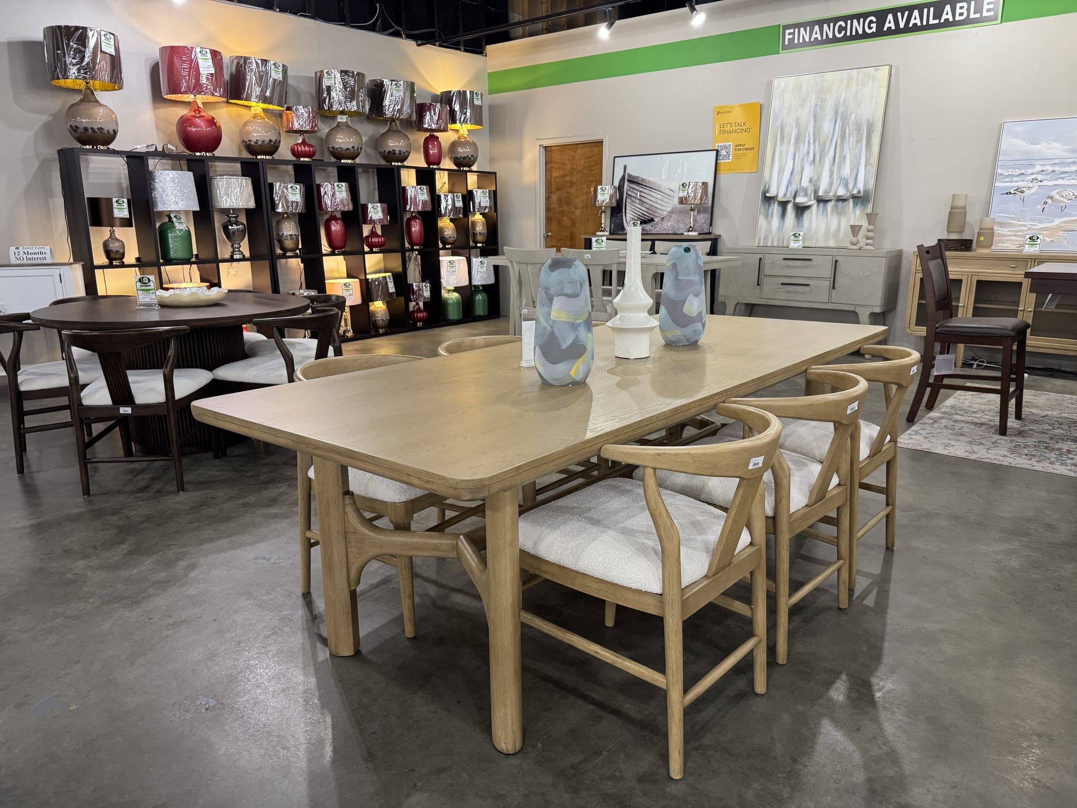 Light oak dining table with woven-back chairs, staged with lamps behind it